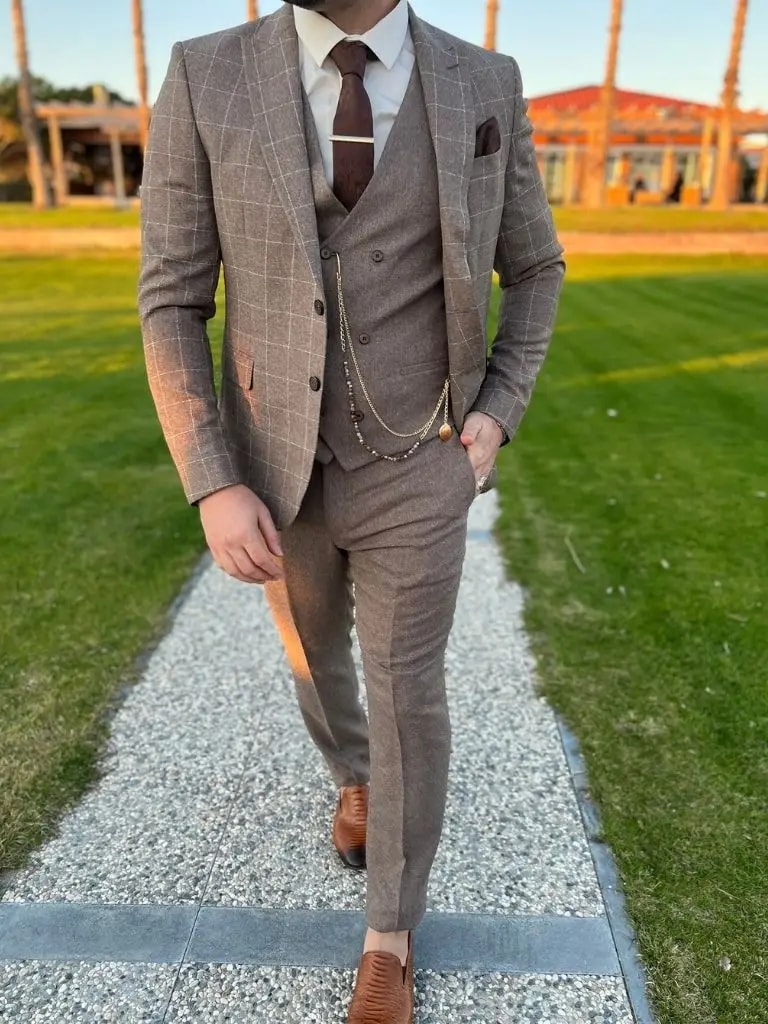 Homme en costume marron à carreaux marchant dans un jardin